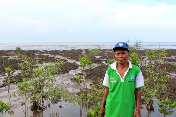 Samsuri standing with mangrove saplings and the ocean in the background