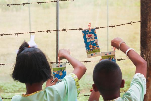 A photo taken from the back of two children hanging milk cartons on a fence