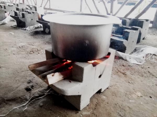 A basin heats over a small concrete stove burning small amounts of wood