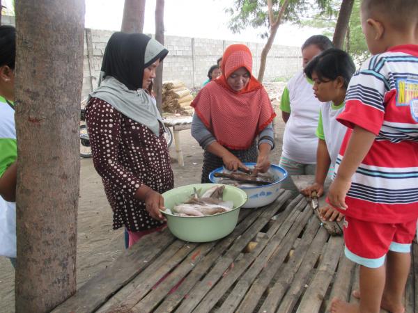 A group of women get ready to clean the two buckets of fish on the table.