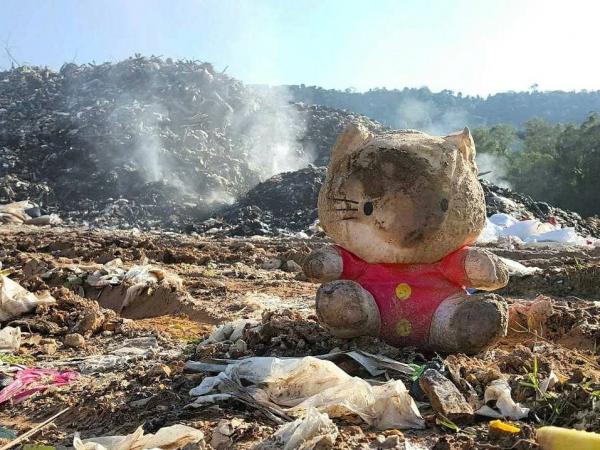 A charred Hello Kitty doll in front of a mountain of burning trash