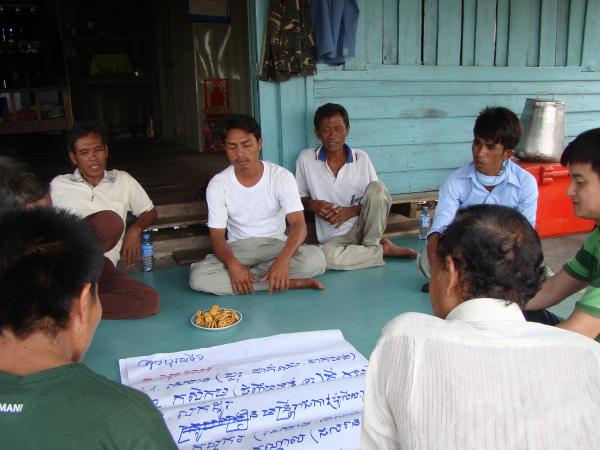 A group of community members sit on the floor around a large poster with notes